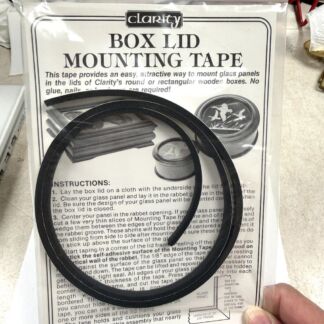 Clarity Box Lid Mounting Tape packaging with two black circular rubber strips laid over instruction sheet for mounting glass panels in box lids.